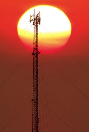 Antenna and cellular tower on blurred big colorful sun background.の写真素材