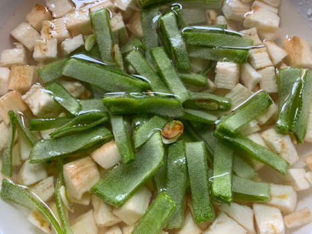 Sliced broad beans and raw plantain cubes soaked in water on a white dish