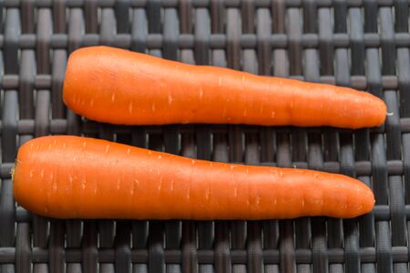 Pair long fresh raw carrot on brown plastic rattan weave table. close up.  の写真素材