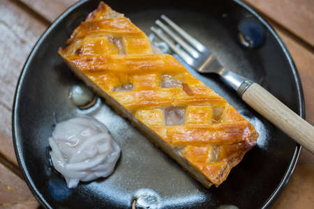 One piece coconut tart large is placed on a black plate. Looks very appetizing, on a wooden table.