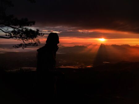 silhouette Alone woman Standing Live on the mountain In the midst of nature While the sun is rising. In the morning the sun shines.の写真素材