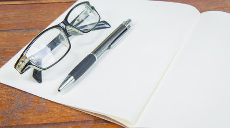 open notebook with pen and glasses on a wooden backgroundの写真素材