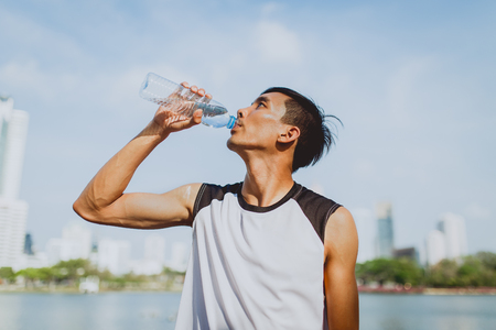 Sports man drinking water after exercising on background of public park.の写真素材