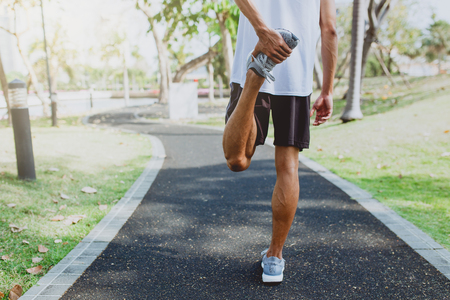 Young man stretching bodies, warming up for jogging in public park.の写真素材