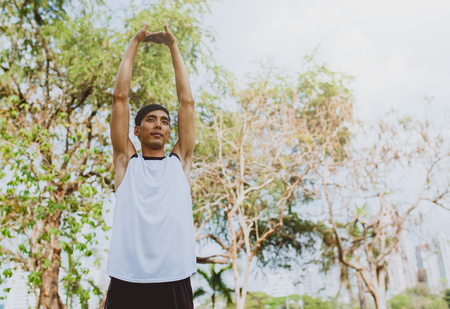 Young man stretching bodies, warming up for jogging in public park.の写真素材