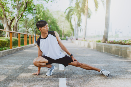 Young man stretching bodies, warming up for jogging in public park.の写真素材