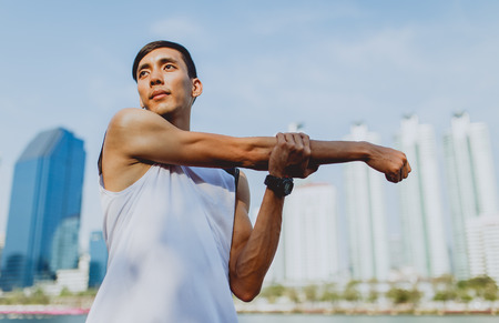 Young man stretching bodies, warming up for jogging in public park.の写真素材