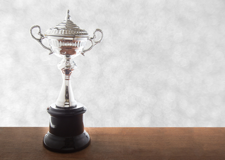 Silver trophy on wooden table over abstact white bokeh background. Winning awards with copy space.の写真素材