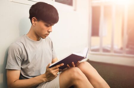 Young handsome asian man reading book at room balcony in free time from working at home, Knowledge and learning concept.の写真素材
