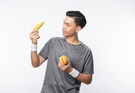 Young handsome asian sport man holding banana and hamburger with smiling isolated on white background.の写真素材