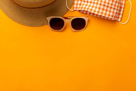 Summer background with beach accessories - straw hat, sunglasses, mask to prevent  on vibrant orange background top view with copy space.の写真素材