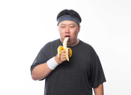 Young Asian funny fat sport man eating banana isolated on white background. Healthy lifestyle concept.の写真素材