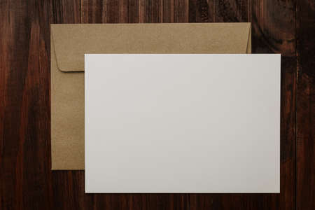 Blank white card template with kraft brown envelope on wooden background.