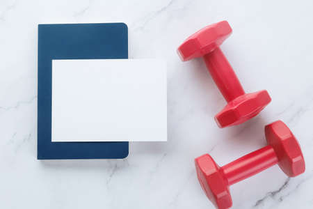 Blank white paper note and dumbells on white marble background. Sport flat lay, Healthy lifestyle and diet concept.の写真素材