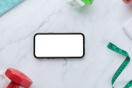 Smartphone with blank screen and fitness equipments on white marble background. Sport flat lay,...