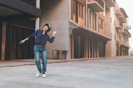 Happy young asian woman listening to music and having fun with headphones via smartphone on the street.の写真素材