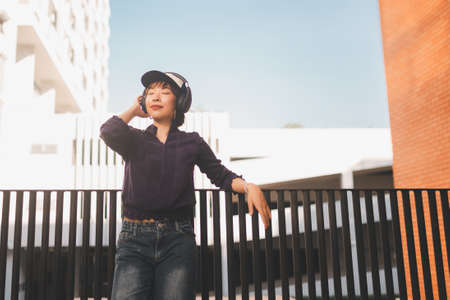 Happy young asian woman listening to music and having fun with headphones on the street.の写真素材