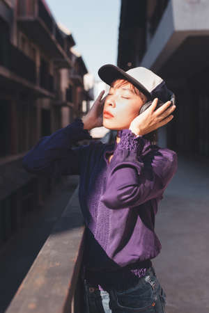 Happy young asian woman listening to music with headphones on the street.