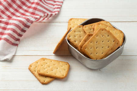 Cracker cookies in a stainless steel bowl with tablecloth on white wooden table background.の写真素材