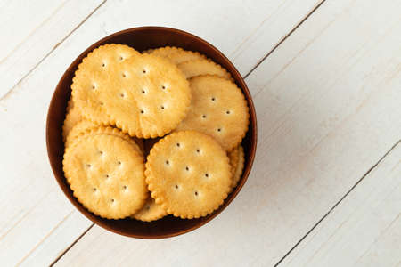 Rounded cracker cookies in a wooden bowl on white wooden table background.