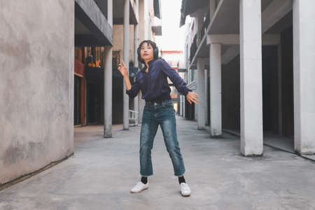 Happy young asian woman listening to music and having fun with headphones on the street.