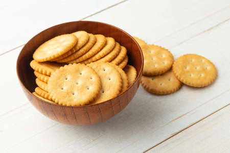 Rounded cracker cookies in a wooden bowl on white wooden table background.の写真素材