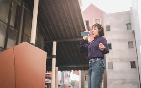 Happy young asian woman listening to music and having fun with headphones via smartphone on the...