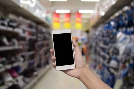 hand hold and touch screen smart phone, on blurred photo of Supermarket store on background with...