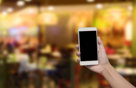 blurred image hand hold and touch screen smart phone on abstract restaurant with abstract bokeh lightの写真素材