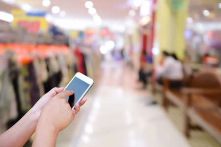 blurred image hand hold and touch screen smart phone on abstract people shopping in supermarketの写真素材