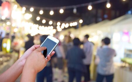 blurred image hand hold and touch screen smart phone and food at night festival with bokeh...