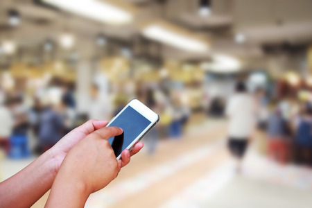 blurred photo and smartphone on food center at shopping mall and people with bokehの写真素材