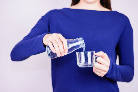 Woman in blue dress pouring water into  glass,glare on bottle and glass.Selective focus at hand holding bottle.の写真素材