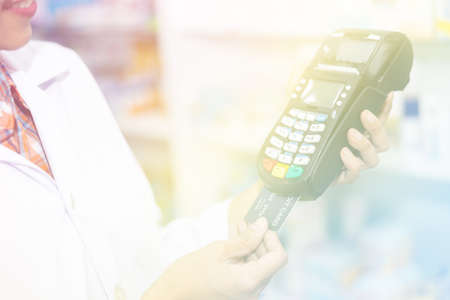 credit card machine on holding hand female pharmacist in pharmacy store Thailand pastel picture style processの写真素材