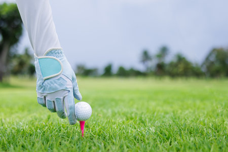 close up of hand female asian professional golfer hold golf ball put on tee by glove golf at green golf course, side view shotの写真素材
