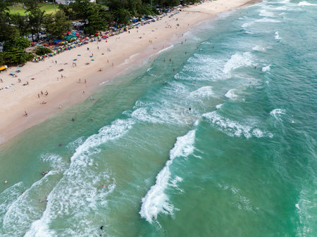 aerial view of the sea waves hitting the beach, tourists play in the sea and sunbathing on the sand beach at surin beach phuket thailand,の写真素材