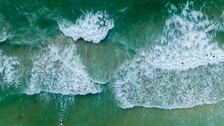 aerial view of the sea waves hitting the beach, tourists play in the sea and sunbathing on the sand beach at surin beach phuket thailand,の写真素材