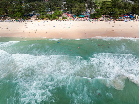 aerial view of the sea waves hitting the beach, tourists play in the sea and sunbathing on the sand beach at surin beach phuket thailand,の写真素材