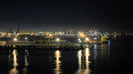 night scene shot commercial port loading and unloading cargo from container ship import and export by crane for distributing goods by trailers transported to customers and dealers, long exposure concept.の写真素材