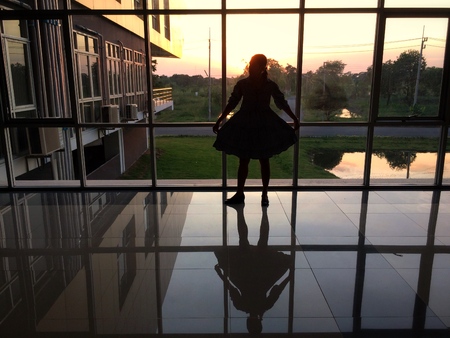 Silhouette of woman stands by looking through the window.の写真素材
