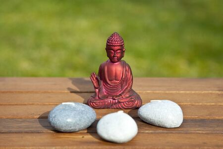 Red Buddha sits surrounded by stones and candles in the sunの写真素材