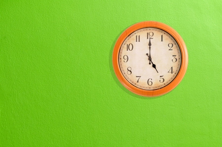 Clock showing 5 o clock on a green wall の写真素材