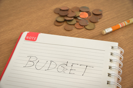 A spiral notebook is noted with budget text a pencil and some coins on wooden tableの写真素材