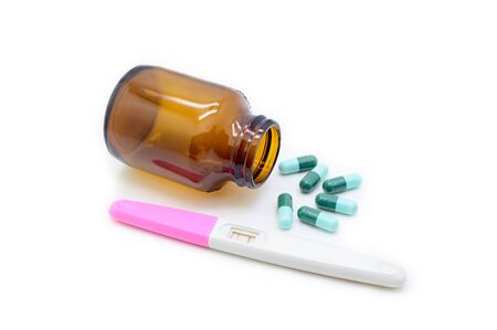 Isolated pills spilling out of glass pill bottle with positive ovulation test on white backgroundの写真素材