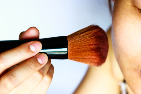 Closeup portrait of a woman applying dry cosmetic tonal foundation on the face using makeup brush.の写真素材