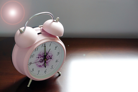 Pink alarm clock on wooden table with lens fair - 6 o'clock in the morning alarm woke me up, it's time to get out of bed and prepare for working day.の写真素材
