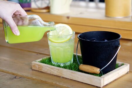 Hand pouring punch lemon juice with soda in glass decorated with slice of lemon - Summer Cocktail or Tropical Mocktail.の写真素材
