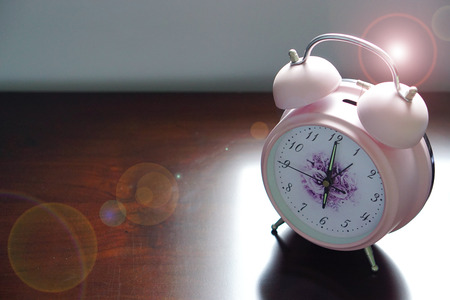 Pink alarm clock and rubber duck on wooden table with lens fair - 6 o'clock in the morning alarm woke me up, it's time to get out of bed and prepare for working day.の写真素材