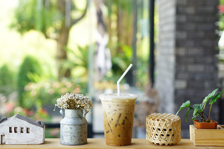 Iced Vanilla Latte - Closeup Plastic glass of iced coffee with milk and vase of Eriocaulon Henryanum Ruhle on blurred background.の写真素材