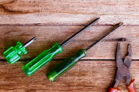 Green screw driver with plier on wooden table background